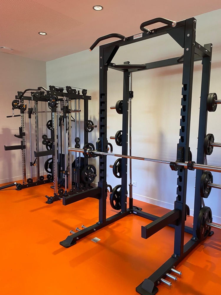 Salle de sport des salariés d’ATI Isolation : rack au premier plan, multistation en fond, sol orange