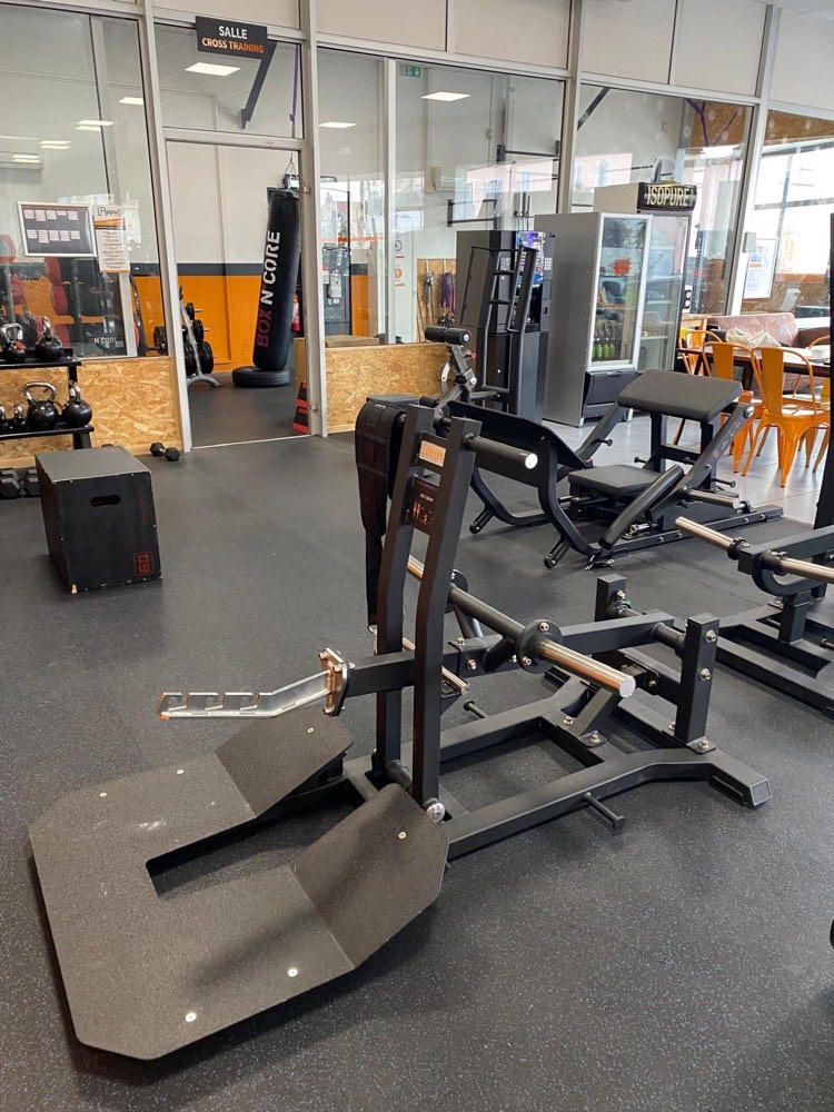 Machine de squat à ceinture installée dans l’espace booty de L’Appart Fitness près de Beaune, devant la salle cross training